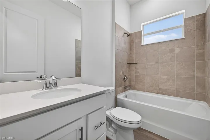 The bathroom features a vanity with a white countertop, a mirror, and a bathtub with tiled walls