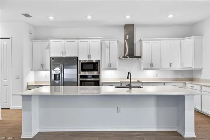The kitchen features white cabinetry, stainless steel appliances, and an island with a sink and faucet