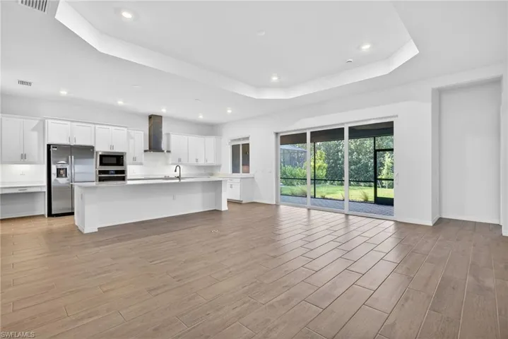 Expansive open-concept living area featuring light-toned flooring, a modern kitchen with white cabinetry, and stainless steel appliances
