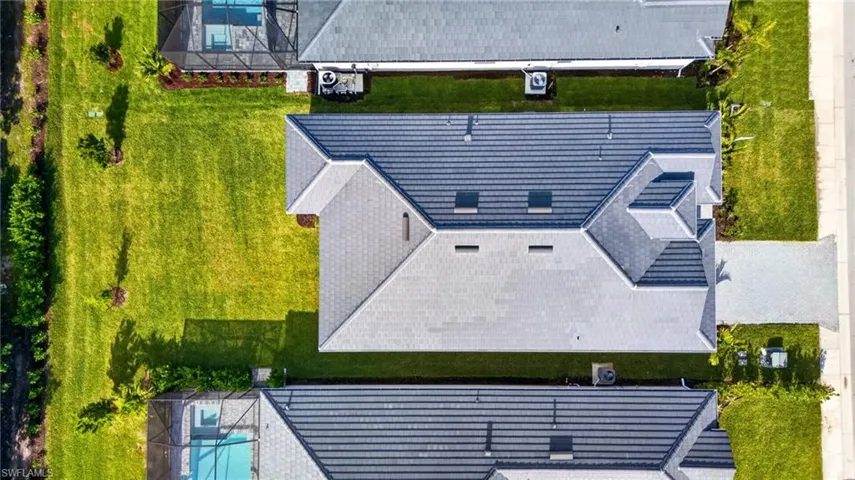 The property features a tile roof, an expansive green lawn, and a light-colored driveway