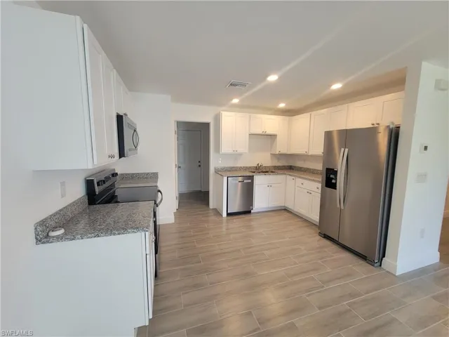 Kitchen featuring white cabinets, stainless steel appliances, recessed lighting, wood finish floors, and dark stone countertops