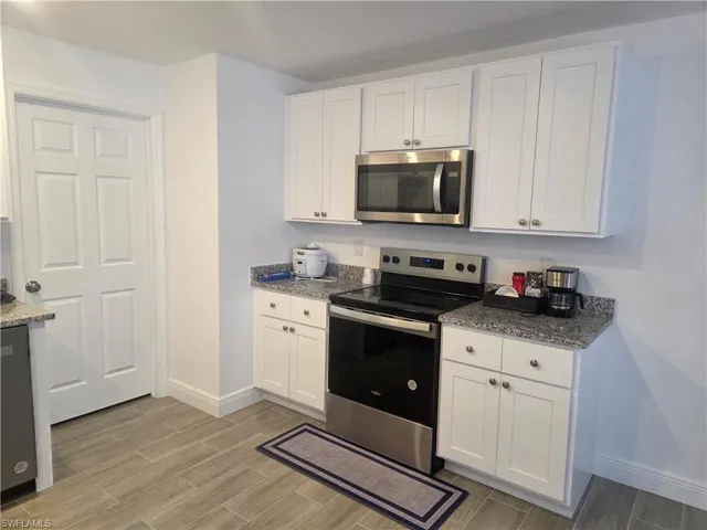 Kitchen with stainless steel appliances, white cabinets, and dark stone counters