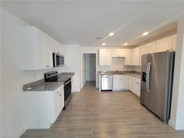 Kitchen with stainless steel appliances, white cabinets, recessed lighting, dark stone counters, and wood finish floors