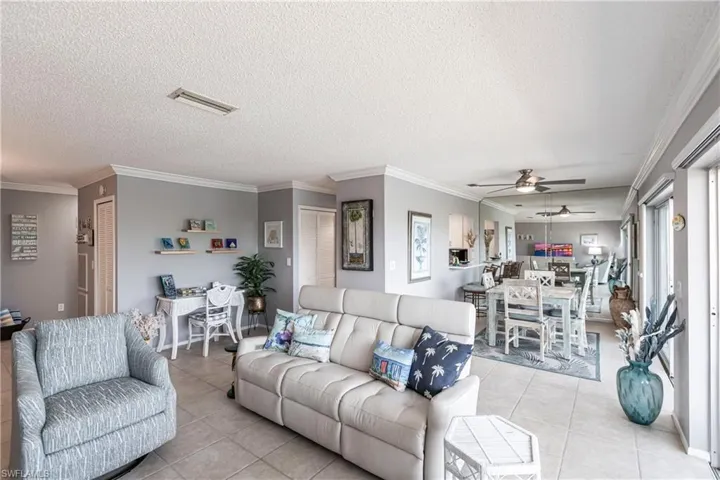 Living area featuring crown molding, light tile patterned floors, a textured ceiling, and ceiling fan