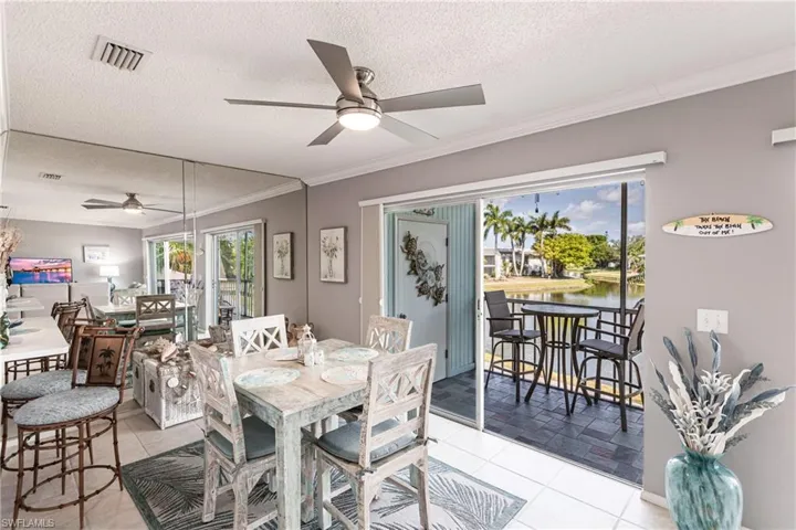 Dining area with a textured ceiling, ceiling fan, a water view, light tile patterned floors, and crown molding
