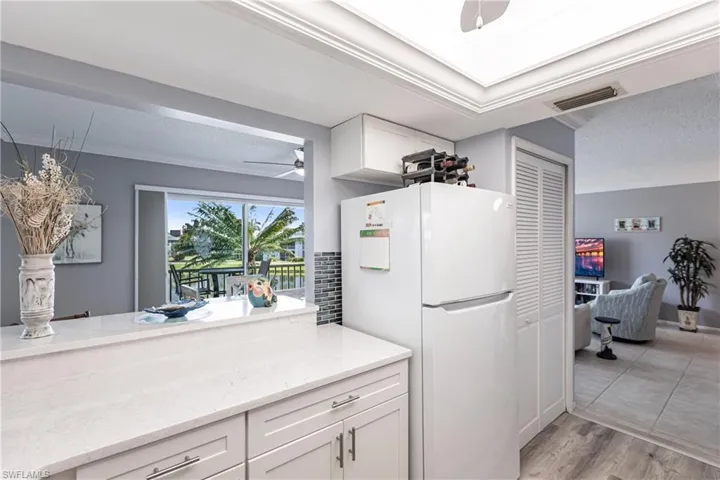 Kitchen with white cabinets, a ceiling fan, freestanding refrigerator, light stone countertops, and crown molding