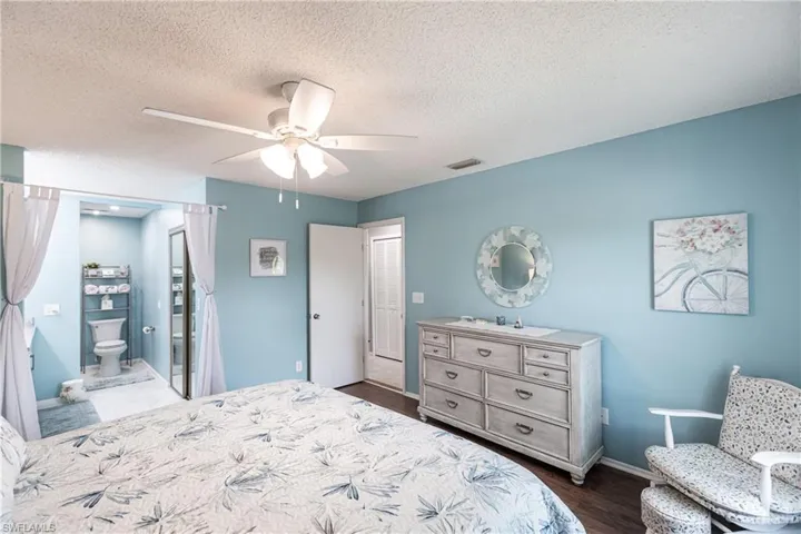 Bedroom featuring a textured ceiling, dark wood-type flooring, ensuite bath, and ceiling fan