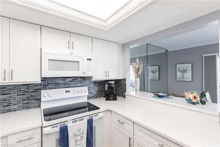 Kitchen with white appliances, white cabinets, light stone counters, and crown molding