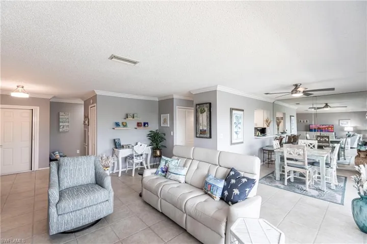 Living area featuring crown molding, light tile patterned floors, a textured ceiling, and a ceiling fan
