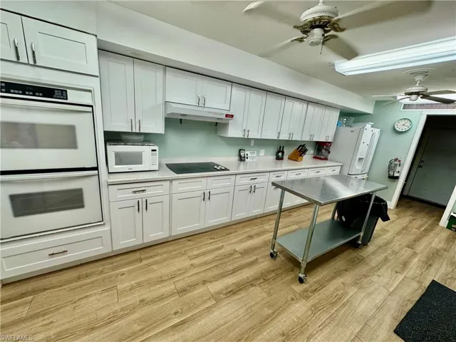 Kitchen with a ceiling fan, white appliances, white cabinets, and light countertops
