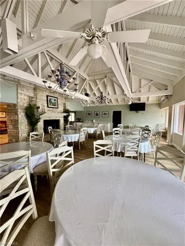 Dining area featuring high vaulted ceiling, dark wood-style flooring, a fireplace, a wooden ceiling with exposed beams, and a ceiling fan
