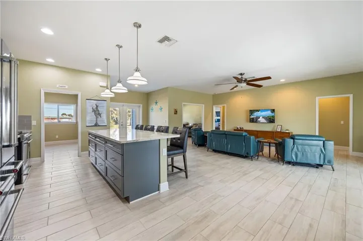 Kitchen featuring a kitchen breakfast bar, light stone countertops, decorative light fixtures, gray cabinetry, and a kitchen island