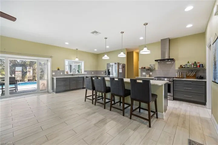 Kitchen with wall chimney exhaust hood, hanging light fixtures, appliances with stainless steel finishes, gray cabinets, and recessed lighting