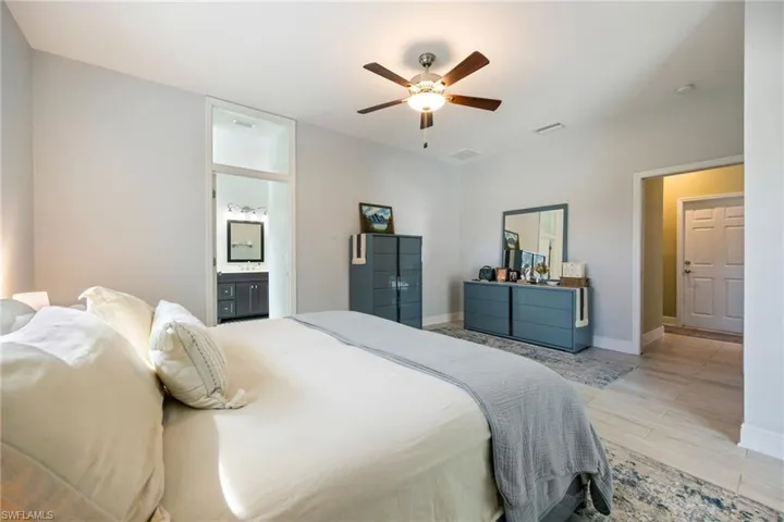 Bedroom with light wood finished floors, ensuite bathroom, and a ceiling fan