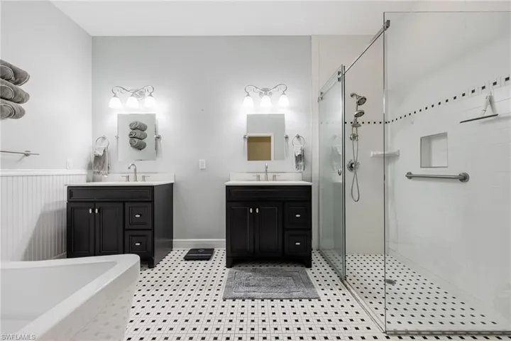 Full bath featuring two vanities, a stall shower, light floors, and a tub