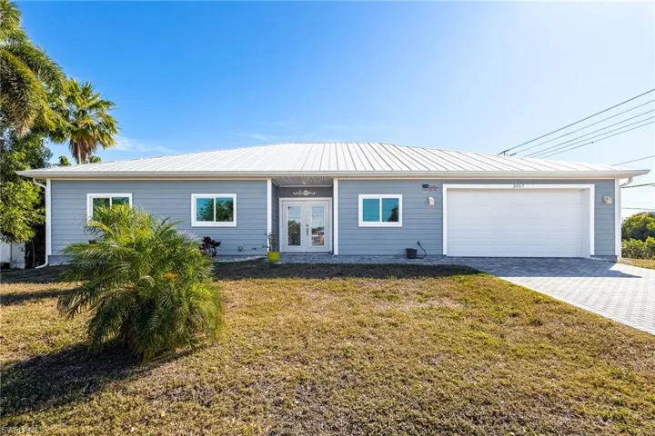 Ranch-style house with a front yard, driveway, an attached garage, and french doors
