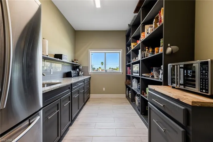 Kitchen with stainless steel appliances, light stone counters, backsplash, and open shelves
