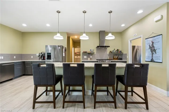 Kitchen with light stone countertops, stainless steel appliances, decorative light fixtures, backsplash, and light wood-style floors