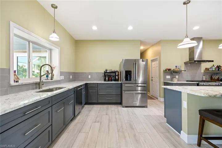 Kitchen with pendant lighting, light stone countertops, stainless steel appliances, wall chimney range hood, and recessed lighting