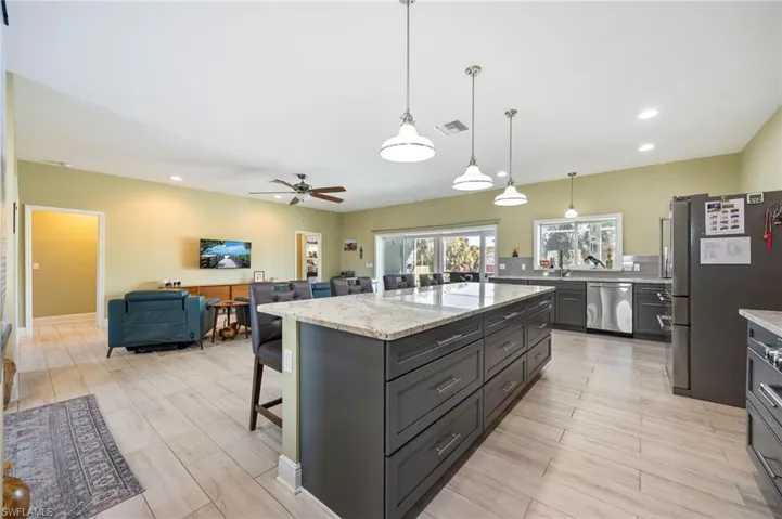 Kitchen featuring recessed lighting, appliances with stainless steel finishes, a kitchen breakfast bar, light stone countertops, and hanging light fixtures