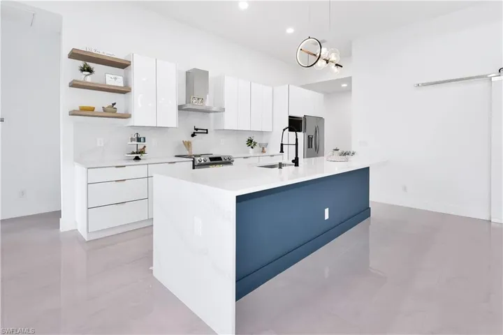 Kitchen with light tile patterned flooring, sink, stainless steel appliances, wall chimney range hood, and white cabinets