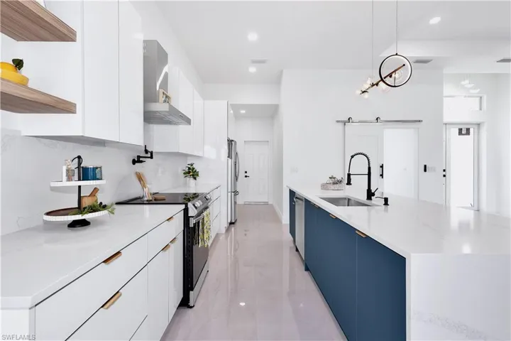 Kitchen with appliances with stainless steel finishes, white cabinetry, wall chimney exhaust hood, pendant lighting, and light tile patterned flooring