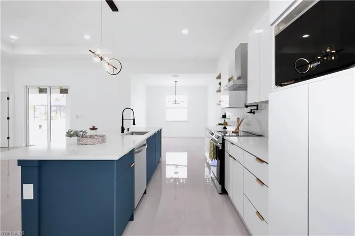 Kitchen with sink, appliances with stainless steel finishes, an island with sink, light tile patterned floors, and hanging light fixtures