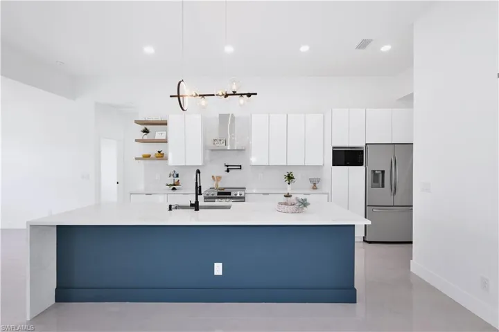 Kitchen featuring appliances with stainless steel finishes, decorative light fixtures, backsplash, white cabinetry, and a center island with sink