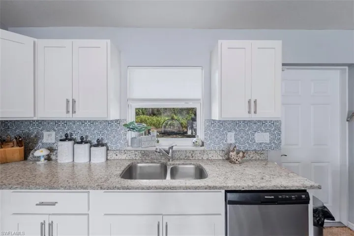 Kitchen with white cabinetry, dishwasher, and light stone countertops