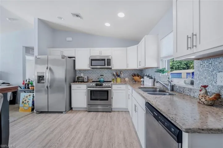 Kitchen with stainless steel appliances, white cabinets, tasteful backsplash, light stone counters, and vaulted ceiling