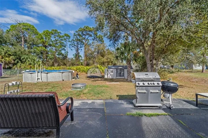 View of patio with an outdoor pool, a storage unit, area for grilling, and view of scattered trees