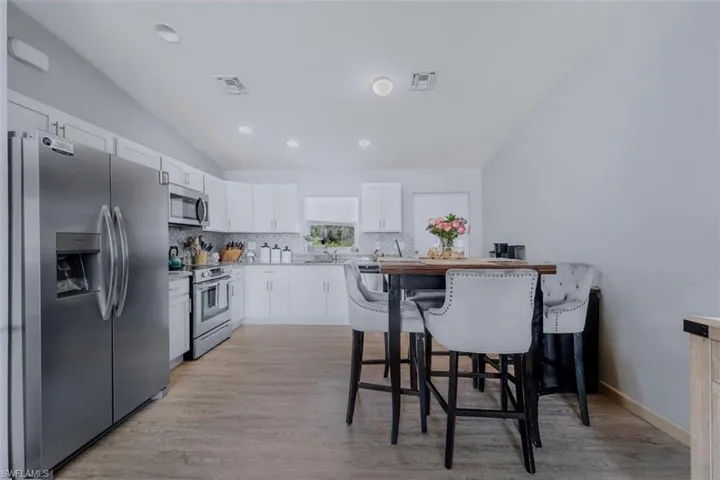 Kitchen with stainless steel appliances, white cabinets, a kitchen bar, light wood-style flooring, and tasteful backsplash