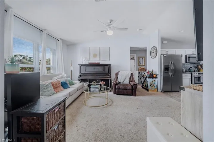 Living area featuring vaulted ceiling, light colored carpet, and a ceiling fan
