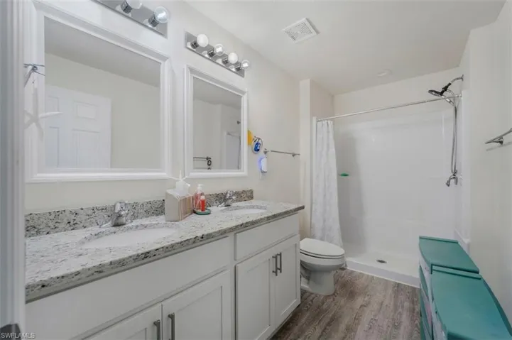Full bath featuring a stall shower, double vanity, and dark wood finished floors