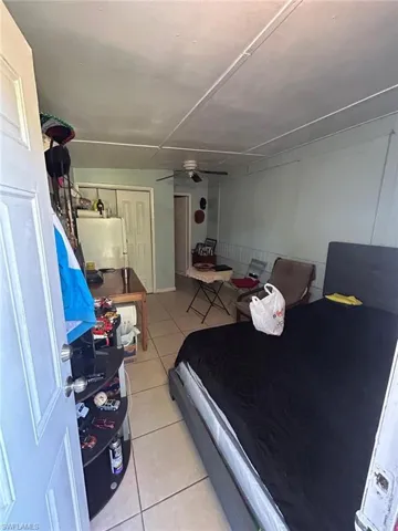 Bedroom with light tile patterned floors, fridge, and a ceiling fan