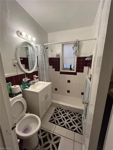 Full bathroom with tile walls, tile patterned flooring, a shower stall, vanity, and a wainscoted wall