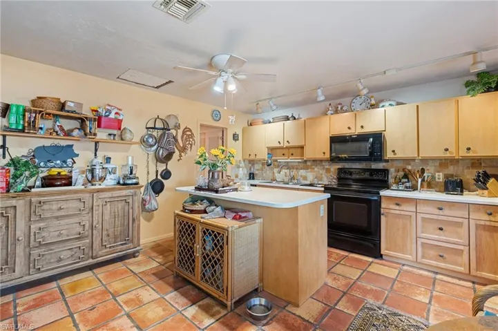 Kitchen featuring light countertops, visible vents, backsplash, light brown cabinets, and black appliances