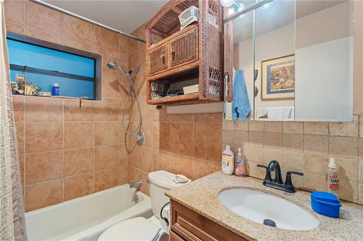 Bathroom featuring shower / bath combination, toilet, backsplash, vanity, and tile walls