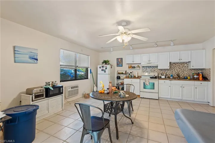 Kitchen with white appliances, light tile patterned flooring, backsplash, and a wall mounted AC