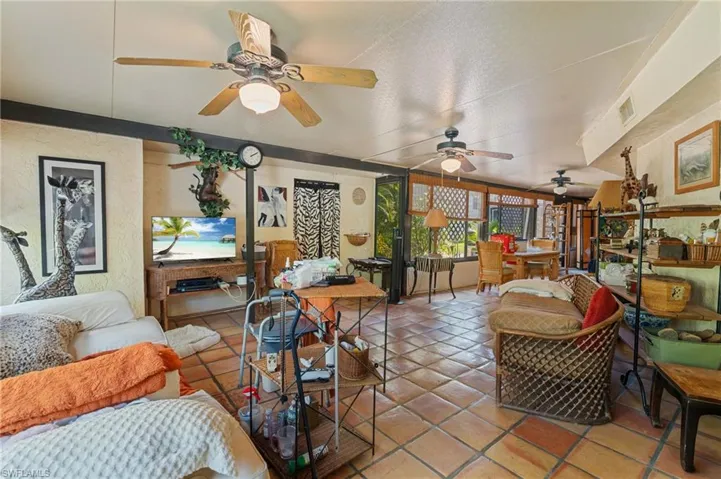 Tiled living area featuring visible vents, a textured wall, a sunroom, and a ceiling fan
