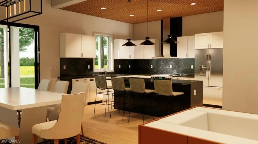 Kitchen with stainless steel fridge, hanging light fixtures, a kitchen breakfast bar, white cabinetry, and a kitchen island