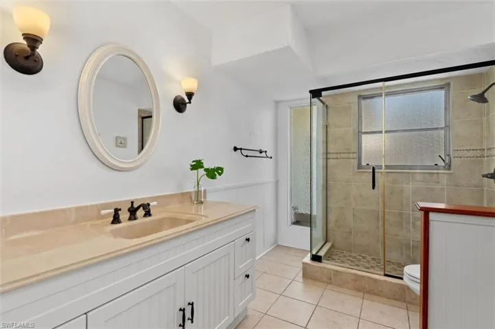 Full bathroom with vanity, a shower stall, tile patterned flooring, and wainscoting