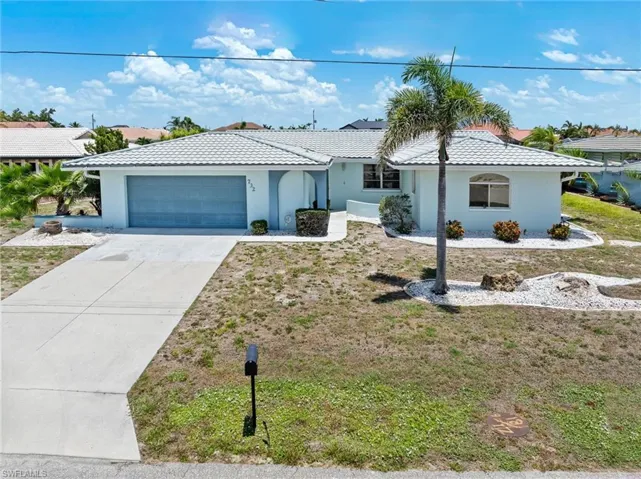 Ranch-style house with stucco siding, driveway, an attached garage, a tiled roof, and a front yard