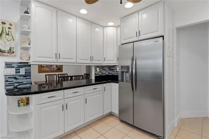 Kitchen with open shelves, stainless steel fridge, decorative backsplash, white cabinets, and recessed lighting