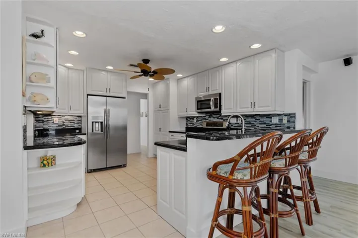 Kitchen with open shelves, stainless steel appliances, a peninsula, decorative backsplash, and recessed lighting