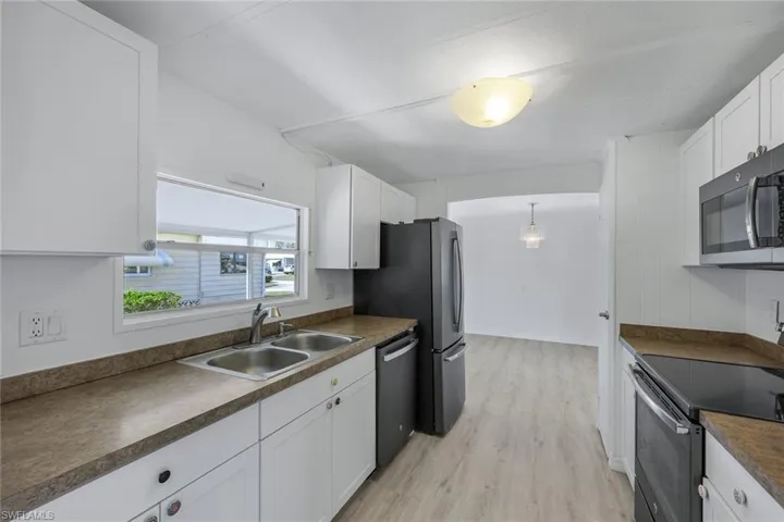 Kitchen with stainless steel appliances, white cabinetry, sink, hanging light fixtures, and light hardwood / wood-style flooring