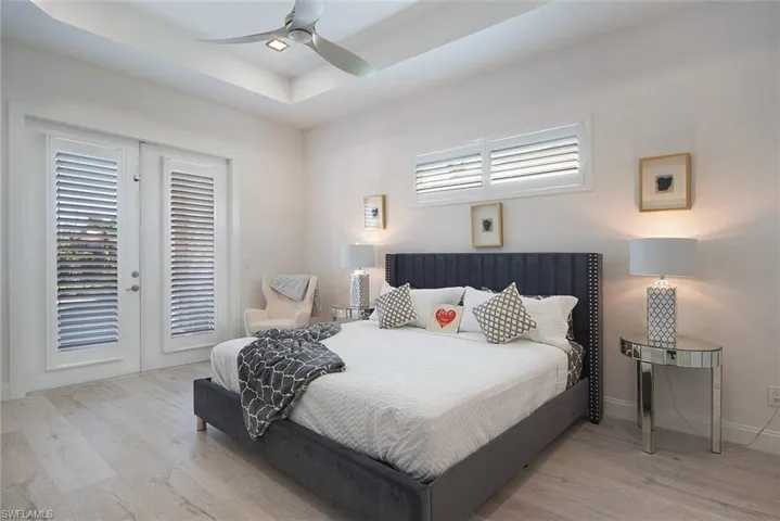 Bedroom with access to exterior, a raised ceiling, light wood-type flooring, and a ceiling fan