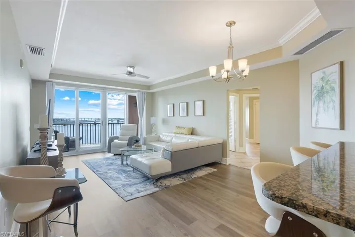 Living room featuring a raised ceiling, a chandelier, a ceiling fan, wood finished floors, and ornamental molding
