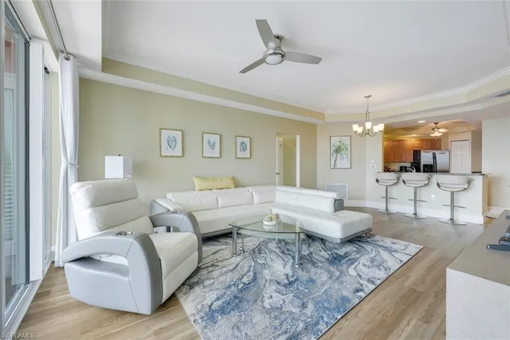 Living room featuring a ceiling fan, a tray ceiling, a chandelier, ornamental molding, and light wood-style flooring