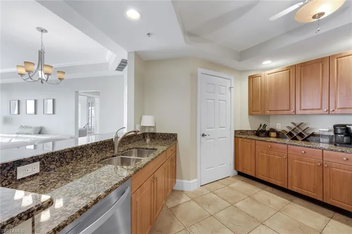 Kitchen featuring a raised ceiling, a sink, dark stone countertops, hanging light fixtures, and stainless steel dishwasher